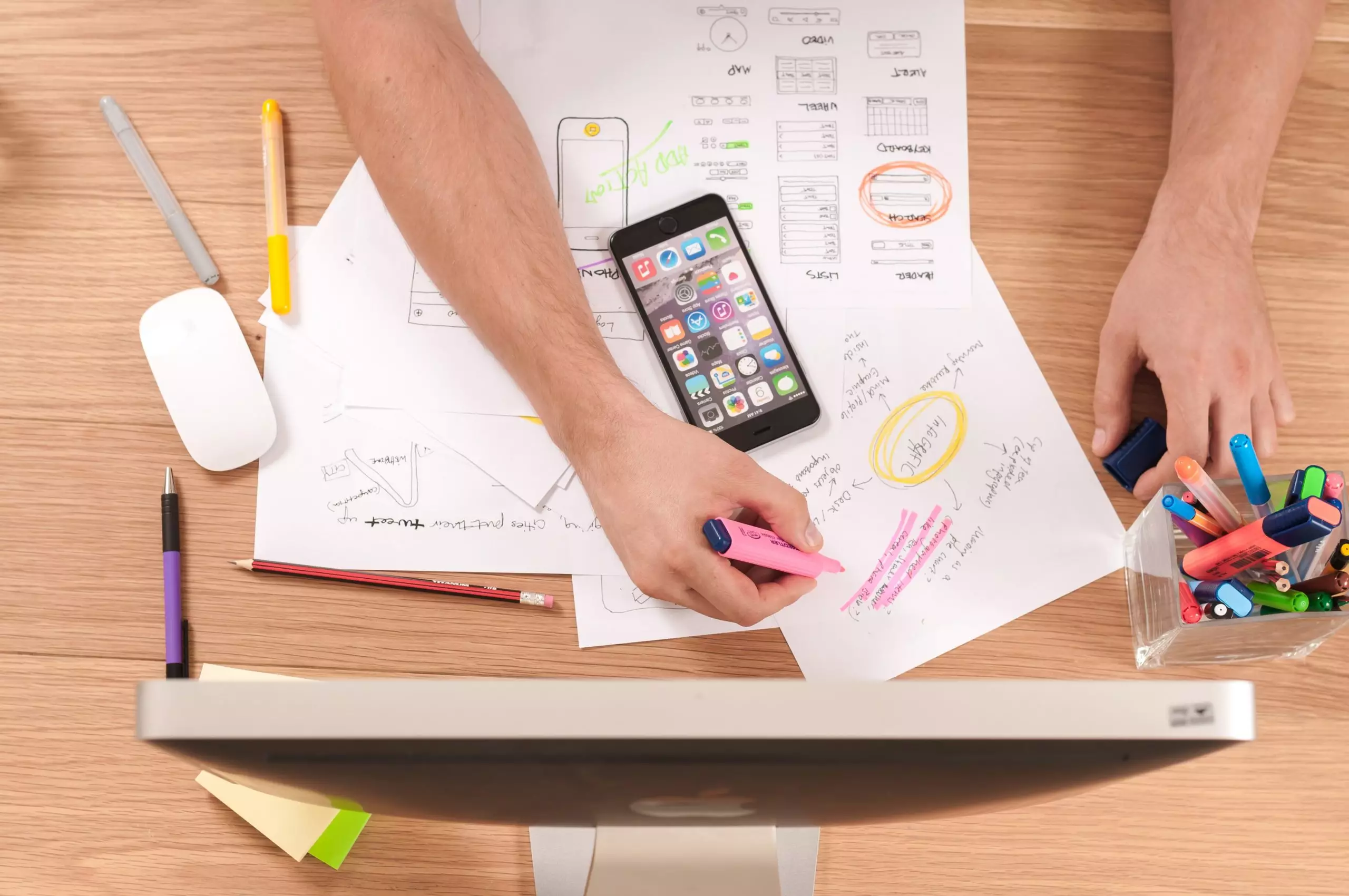Mains sur un bureau avec maquettes papier, smartphone et croquis d'architecture web
